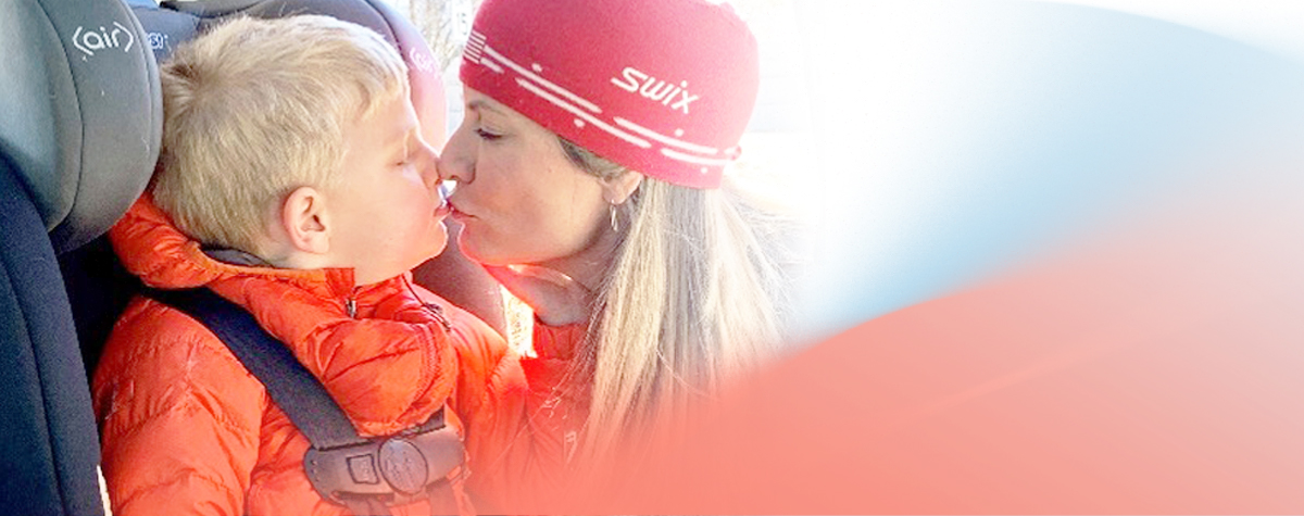 Mother kissing her son while he sits in his carseat