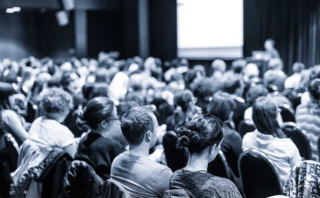 Black and white photo of an audience watching a presenter on stage